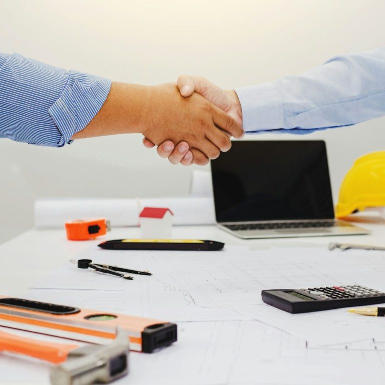collaboration, partenariat Poignée de main entre deux personnes avec des outils et un ordinateur portable sur la table.