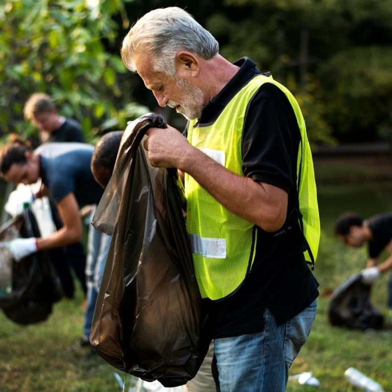 accès aux personnes âgées Homme âgé en gilet fluo recueillant des déchets lors d'un nettoyage en plein air.